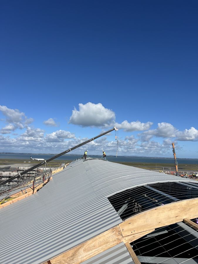 Project Unite roofers on the curved standing seam roof of the domestic processor, with a crane and the runway behind