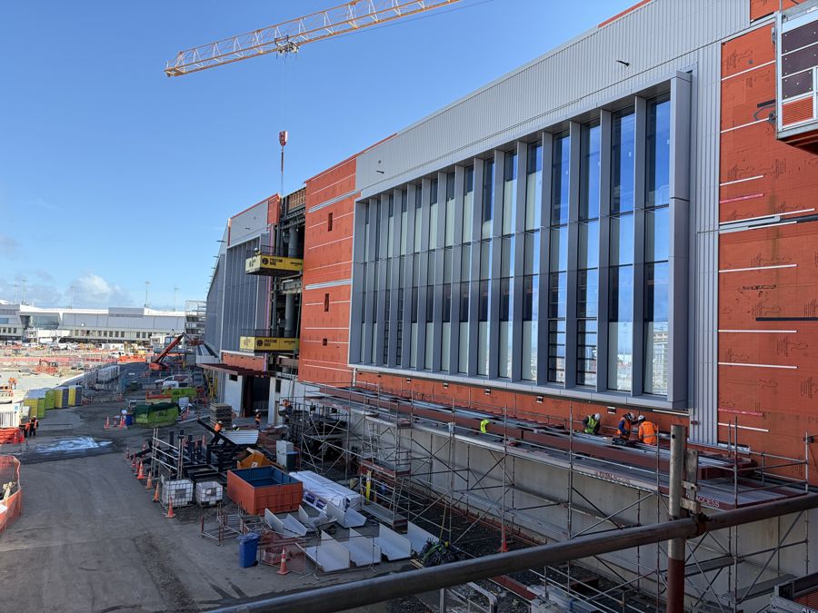 New façade with vertical aluminium fins going up at Auckland Airport, WP1, with scaffolding and site works below